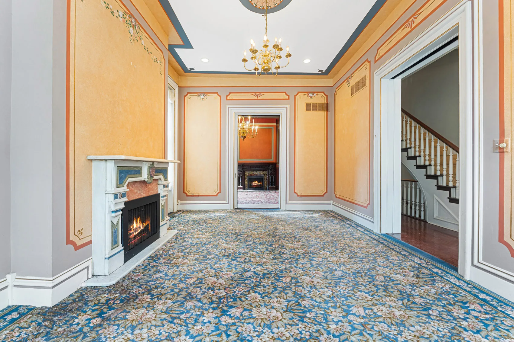 Main-level interior with decorative painted walls, chandeliers, marble fireplaces, and adjoining rooms