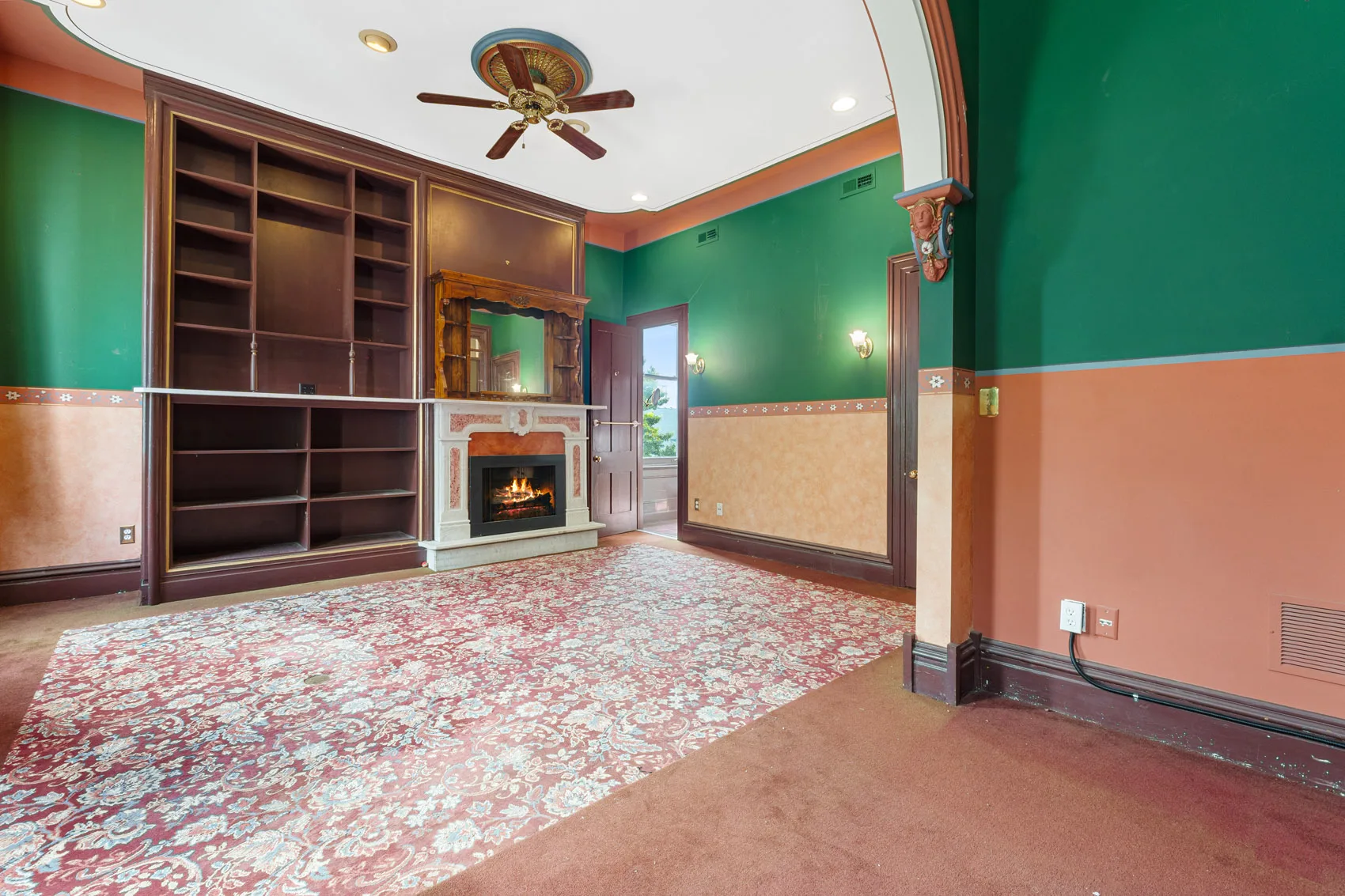 Second-floor parlor with green walls, built-in wood shelving, a marble fireplace, and decorative columns